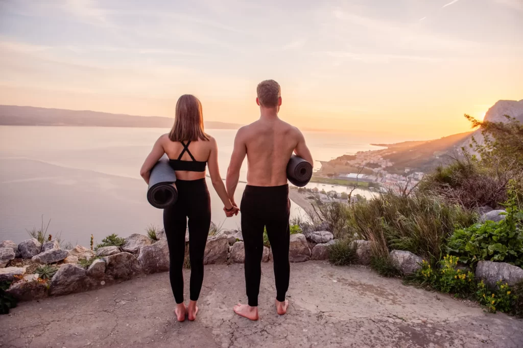 couple holding yoga mats watching coastal sunset utc
